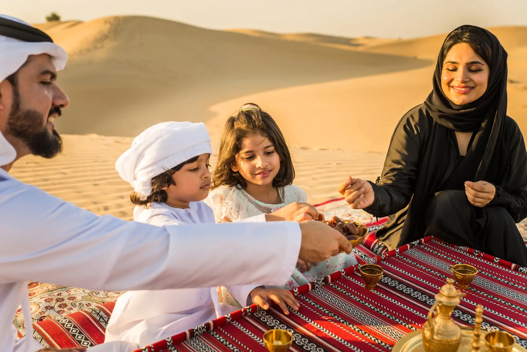 A family sharing Arabic coffee on a rug in the Qatari dunes
